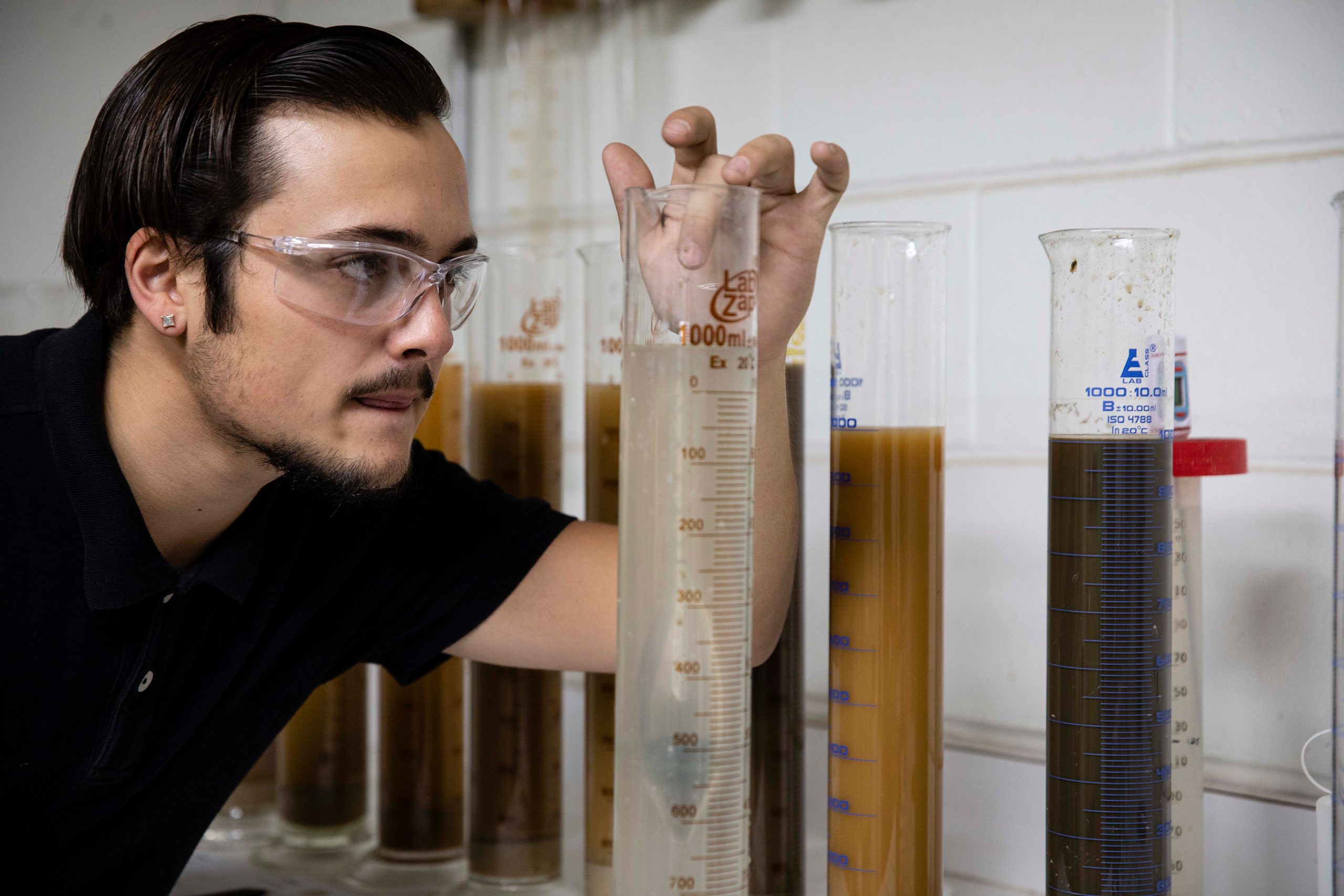 Man with safety glasses leveling a graduated cylinder
